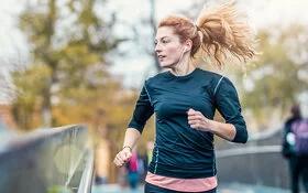 Eine junge Frau joggt über eine Brücke und hört dabei Musik.