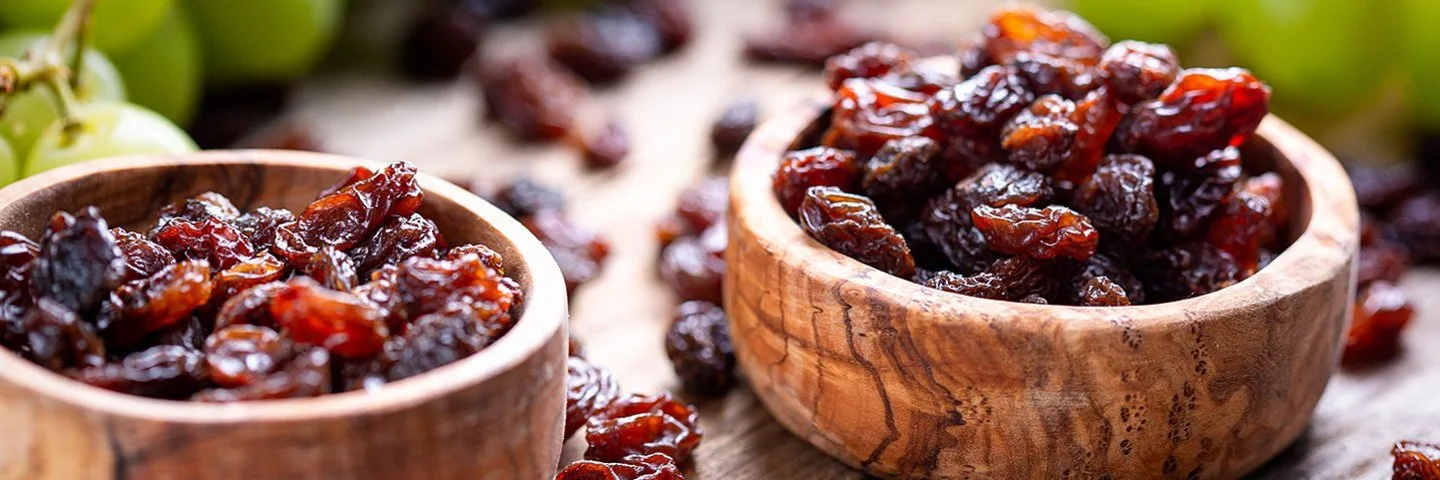 Zwei Holzschalen sind mit Rosinen und Trauben gefüllt und stehen auf einem Tisch.