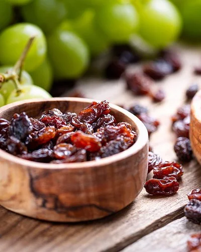 Zwei Holzschalen sind mit Rosinen und Trauben gefüllt und stehen auf einem Tisch.