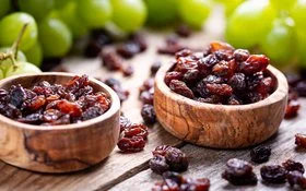 Zwei Holzschalen sind mit Rosinen und Trauben gefüllt und stehen auf einem Tisch.
