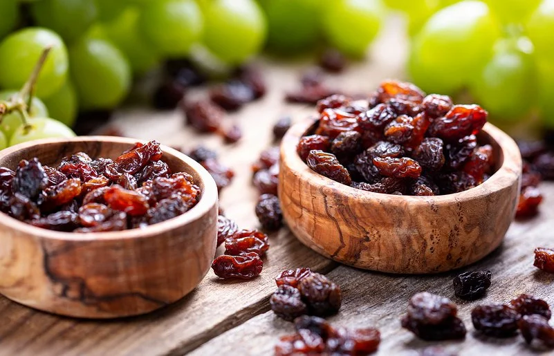 Zwei Holzschalen sind mit Rosinen und Trauben gefüllt und stehen auf einem Tisch.