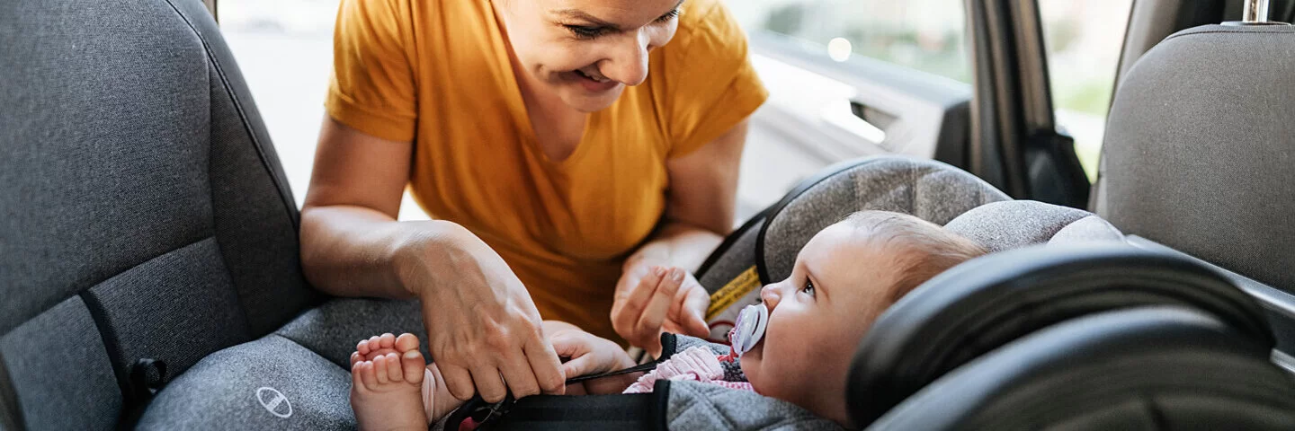 Eine Mutter schnallt lächelnd ihr Baby in Babyschale an, die rückwärtsgewandt eingebaut ist.