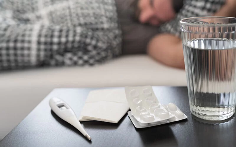 Medikamente gegen Grippe oder Erkältung und Fieberthermometer liegen auf dem Nachttisch.