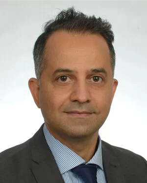 Man sieht das Portrait von einem Mann (Hr. A. Amedi). Er trägt ein hellblaues Hemd mit dunkler Krawatte und Jackett.