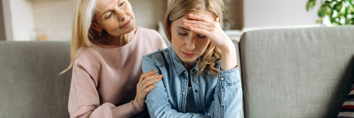 Eine Frau sitzt neben ihrer Angehörigen, die an Depressionen leidet, und legt ihr die Hände auf die Schultern.