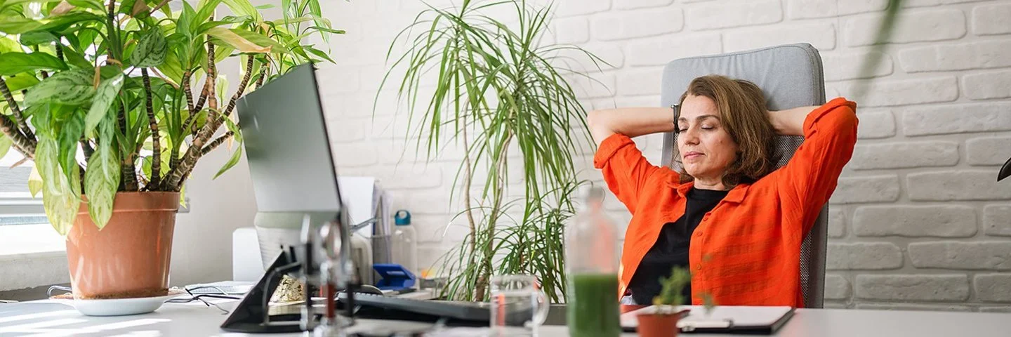 Eine Frau sitzt an einem Schreibtisch und lehnt sich lächelnd zurück.