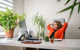 Eine Frau sitzt an einem Schreibtisch und lehnt sich lächelnd zurück.