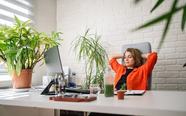 Eine Frau sitzt an einem Schreibtisch und lehnt sich lächelnd zurück.