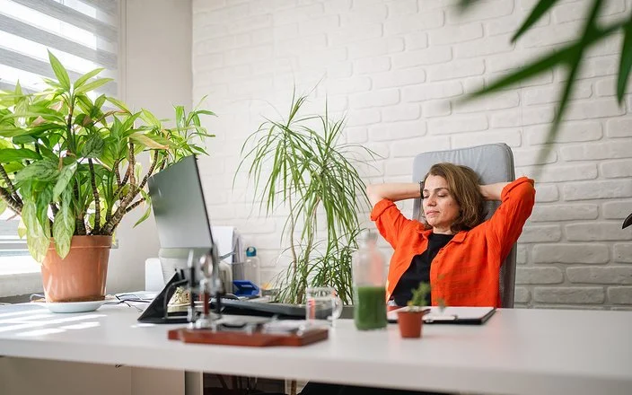 Eine Frau sitzt an einem Schreibtisch und lehnt sich lächelnd zurück.