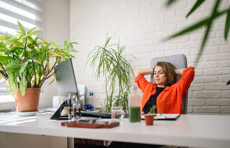 Eine Frau sitzt an einem Schreibtisch und lehnt sich lächelnd zurück.