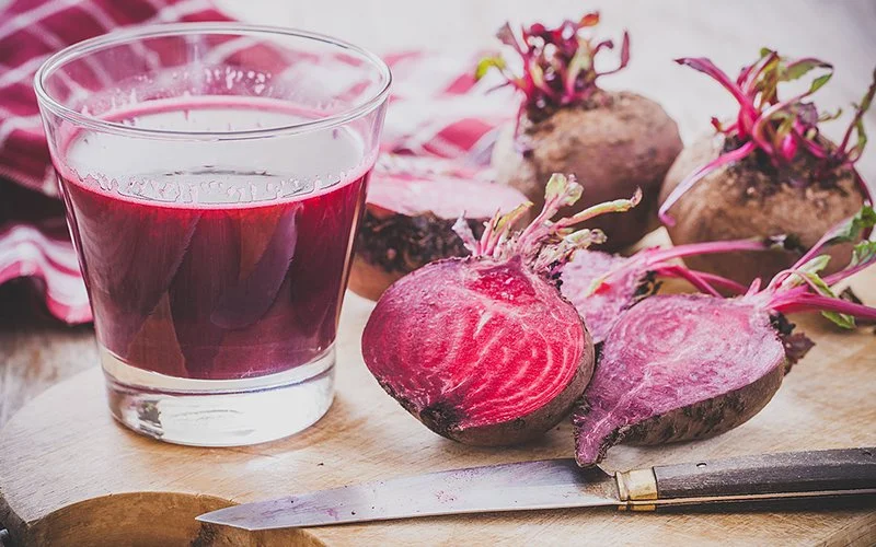 Rote Bete Saft in einem Glas, Rote Bete als Knolle und aufgeschnitten auf einem Holzbrett.