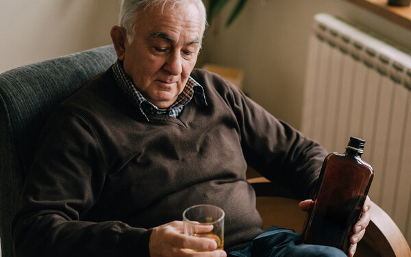 Ein Mann sitzt in einem Sessel und trinkt ein Glas Whiskey.