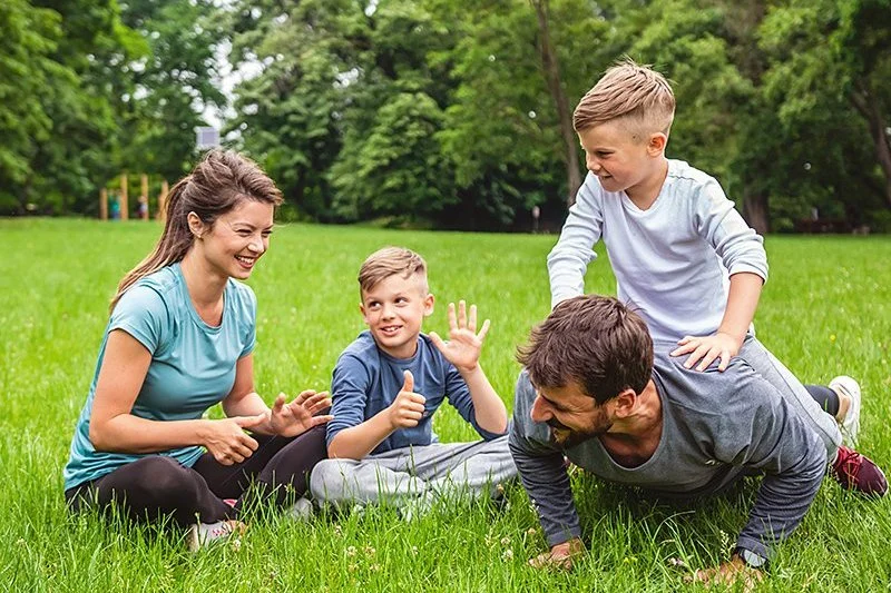 Eine Familie mit zwei Kindern spielt und macht Liegestütze auf einer Wiese im Park