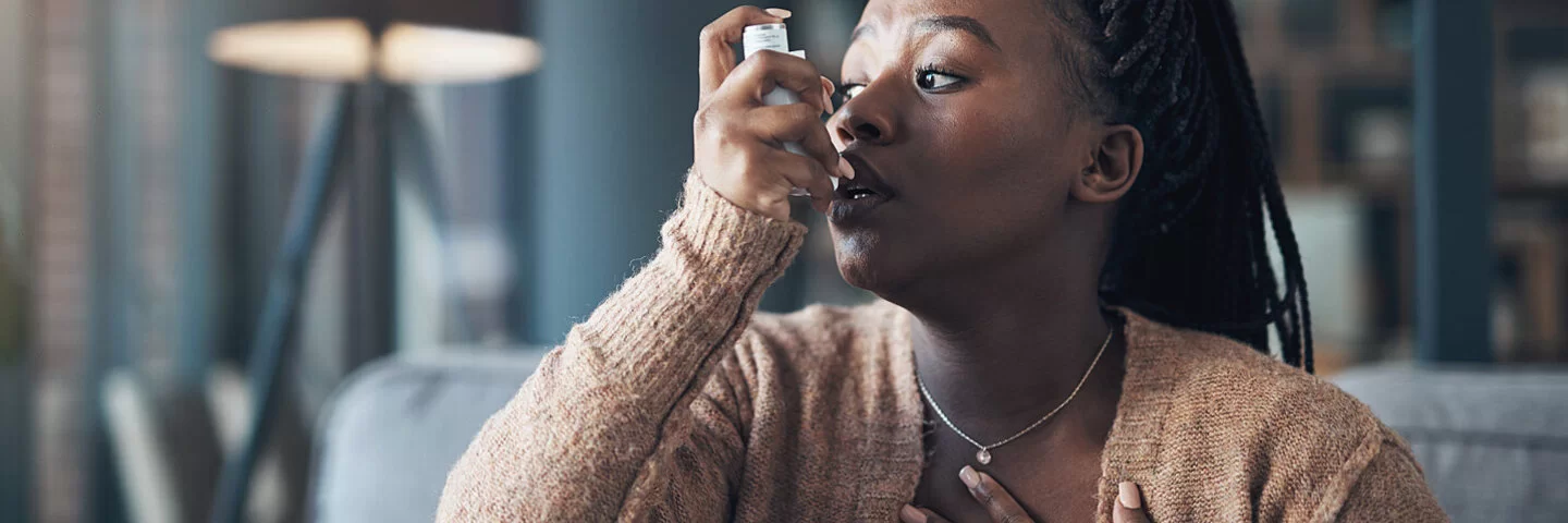 Eine Frau hat einen Asthmaanfall und Atemnot, darum benutzt sie ihr Asthmaspray.