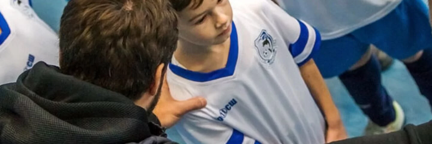 Man sieht wie ein Trainer mit einem kleinen Jungen aus einer Handballmannschaft spricht.