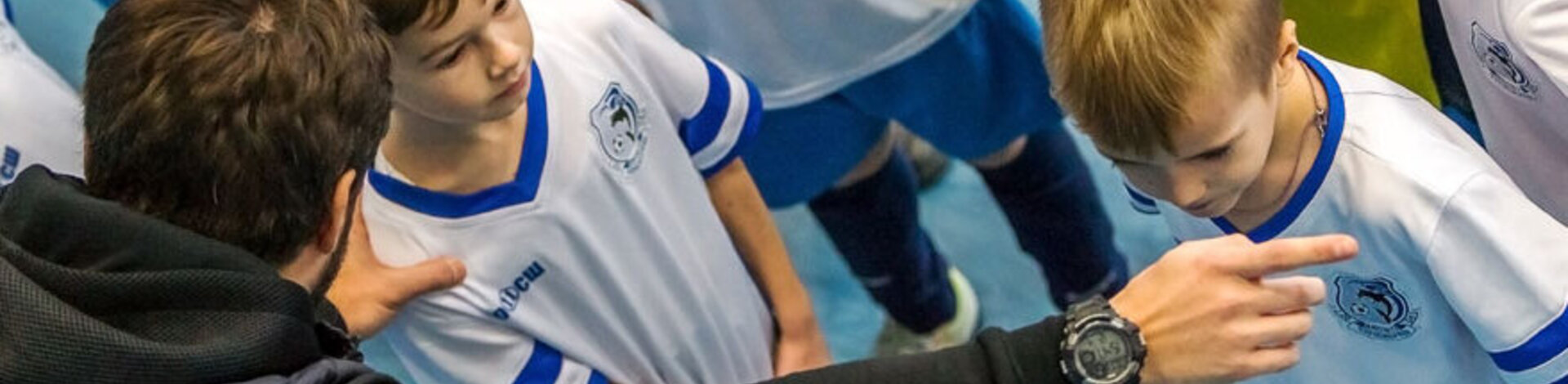 Man sieht wie ein Trainer mit einem kleinen Jungen aus einer Handballmannschaft spricht.