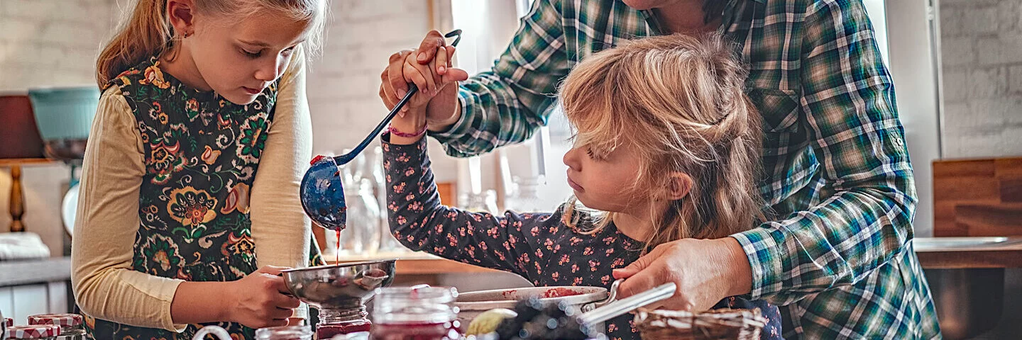 Frau kocht mit zwei kleinen Mädchen Marmelade ohne Zucker.