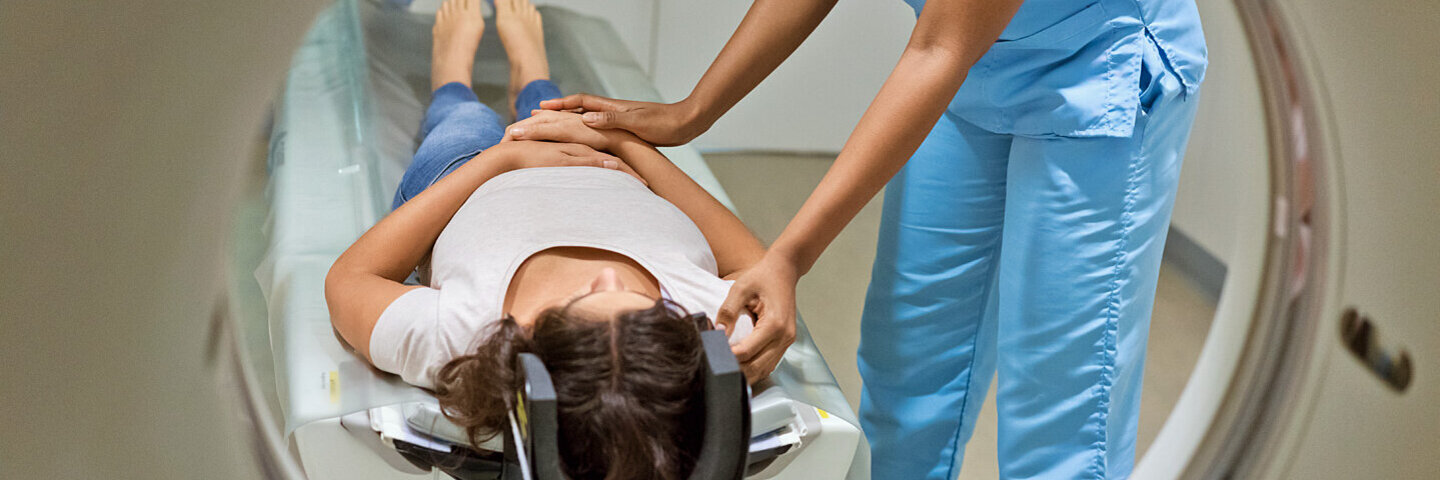 Ärztin schiebt liegende Patientin mit dem Kopf zuerst in die Röhre für eine MRT (Magnetresonanztomografie).