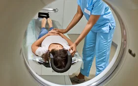 Ärztin schiebt liegende Patientin mit dem Kopf zuerst in die Röhre für eine MRT (Magnetresonanztomografie).