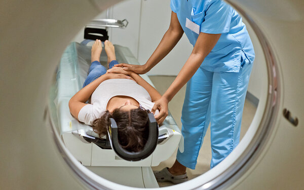 Ärztin schiebt liegende Patientin mit dem Kopf zuerst in die Röhre für eine MRT (Magnetresonanztomografie).