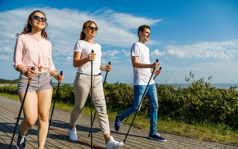 Eine Mutter betreibt Nordic Walking am Meer mit ihren beiden jugendlichen Kindern.