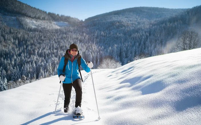 Eine Frau geht lächelnd mit Schneeschuhen durch den Schnee.