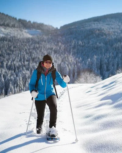 Eine Frau geht lächelnd mit Schneeschuhen durch den Schnee.