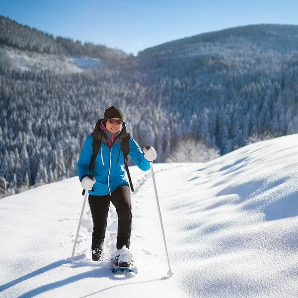 Eine Frau geht lächelnd mit Schneeschuhen durch den Schnee.