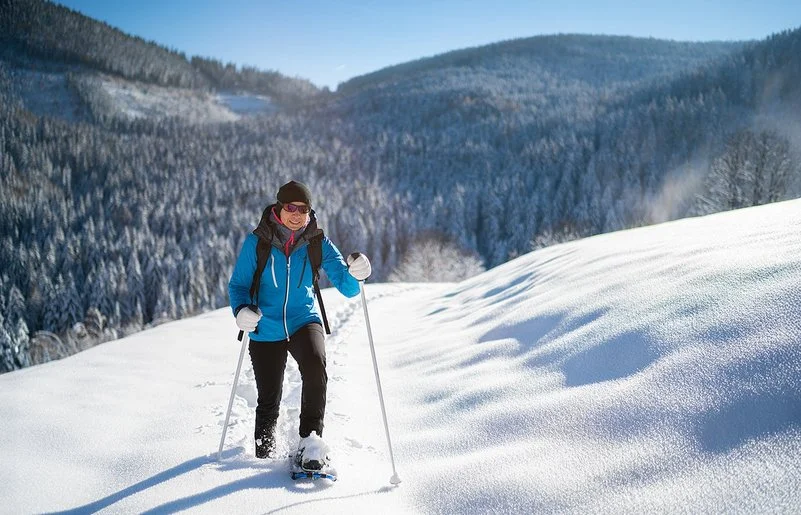 Eine Frau geht lächelnd mit Schneeschuhen durch den Schnee.