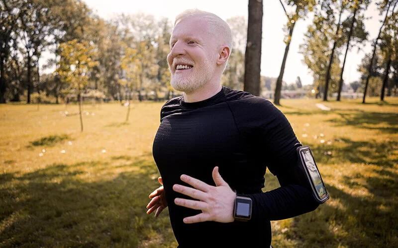 Mann mit Albinismus joggt in schwarzer Sportkleidung durch einen Park.