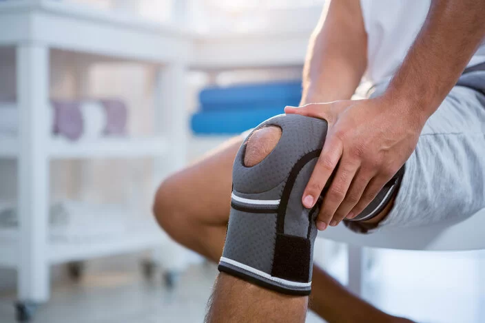 Ein Mann trägt an seinem linken Knie eine Bandage. Er hält mit beiden Händen sein linkes Knie fest.