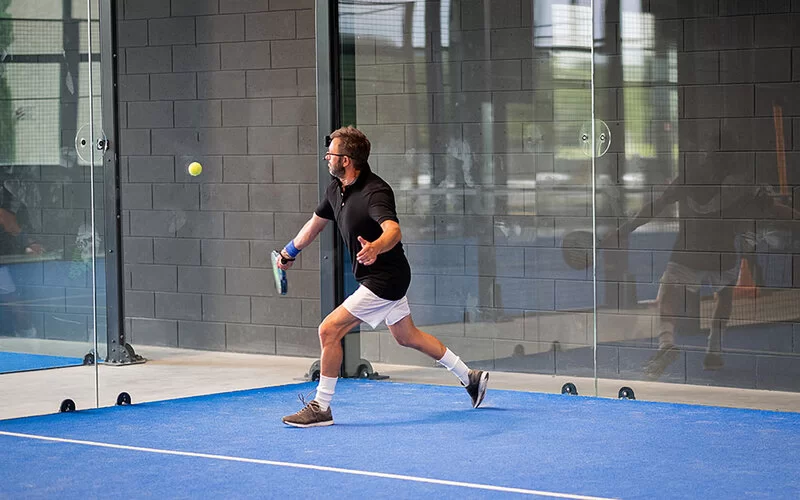 Mann spielt drinnen auf einem blauen Feld Padel.