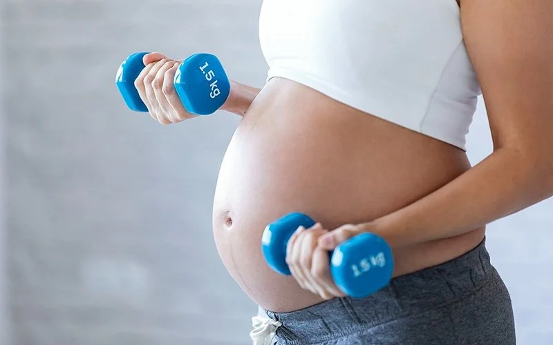 Eine schwangere Frau trainiert mit kleinen Hanteln.