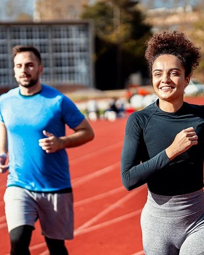 Eine Frau und ein Mann laufen Runden auf dem Sportplatz.
