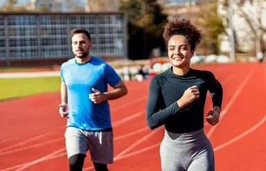 Eine Frau und ein Mann laufen Runden auf dem Sportplatz.