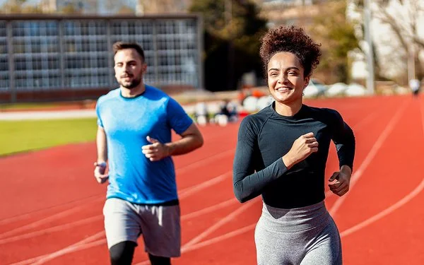 Eine Frau und ein Mann laufen Runden auf dem Sportplatz.