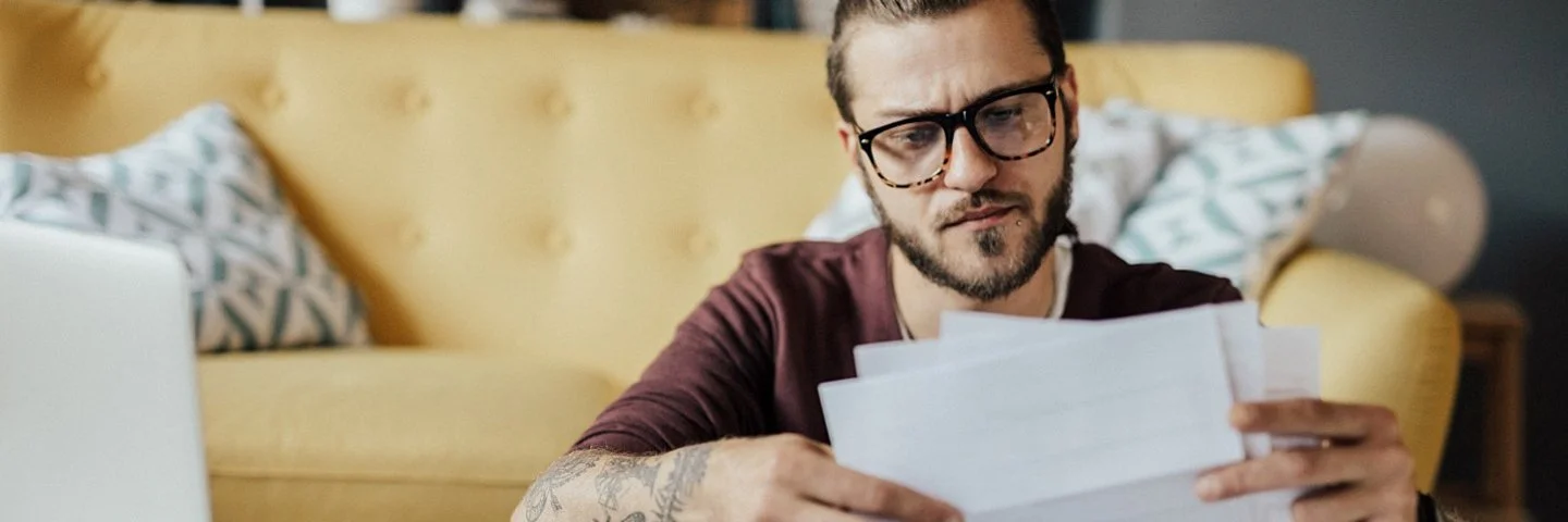 Ein junger Mann sitzt mit Dokumenten am Küchentisch und vergleicht Angebote von gesetzlichen und privaten Krankenversicherungen.