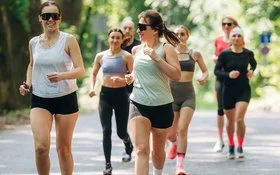 Läuferinnen und Läufer eines Running Clubs joggen gemeinsam auf einer sonnigen Straße durch einen grünen Wald.
