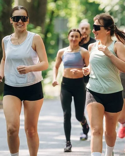 Läuferinnen und Läufer eines Running Clubs joggen gemeinsam auf einer sonnigen Straße durch einen grünen Wald.