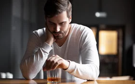 Junger Mann sitzt allein vor seinem Whiskey-Glas – ist das schon eine Sucht?