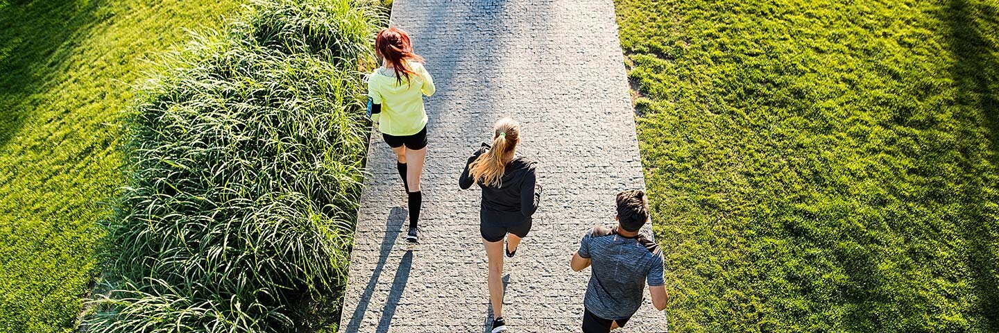 Drei junge Menschen beim Laufen im Park von hinten aus der Vogelperspektve aufgenommen.