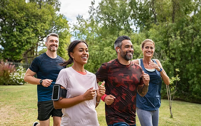 Zwei Frauen und zwei Männer unterschiedlicher ethnischer Herkunft im mittleren Lebensalter joggen fröhlich zusammen im Park.