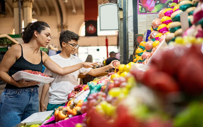 Mutter und Sohn kaufen in einer Markthalle an einem Obststand ein.