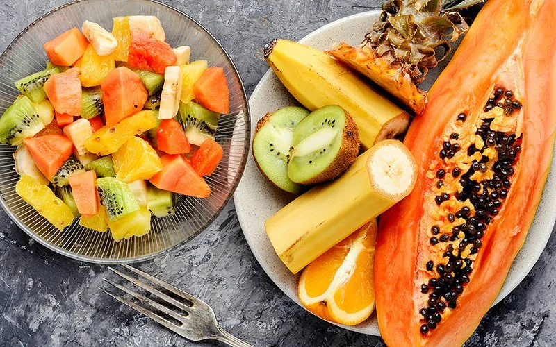 Eine Schüssel mit unzubereitetem Obst steht neben einer Schüssel mit Fruchtsalat.