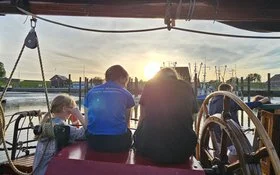 Fünf Menschen auf einem Segelboot bei Sonnenuntergang.
