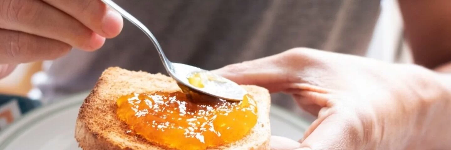 Mann schmiert sich ein Brötchen mit Konfitüre und fragt sich, ob da vielleicht versteckter Alkohol drinsteckt.