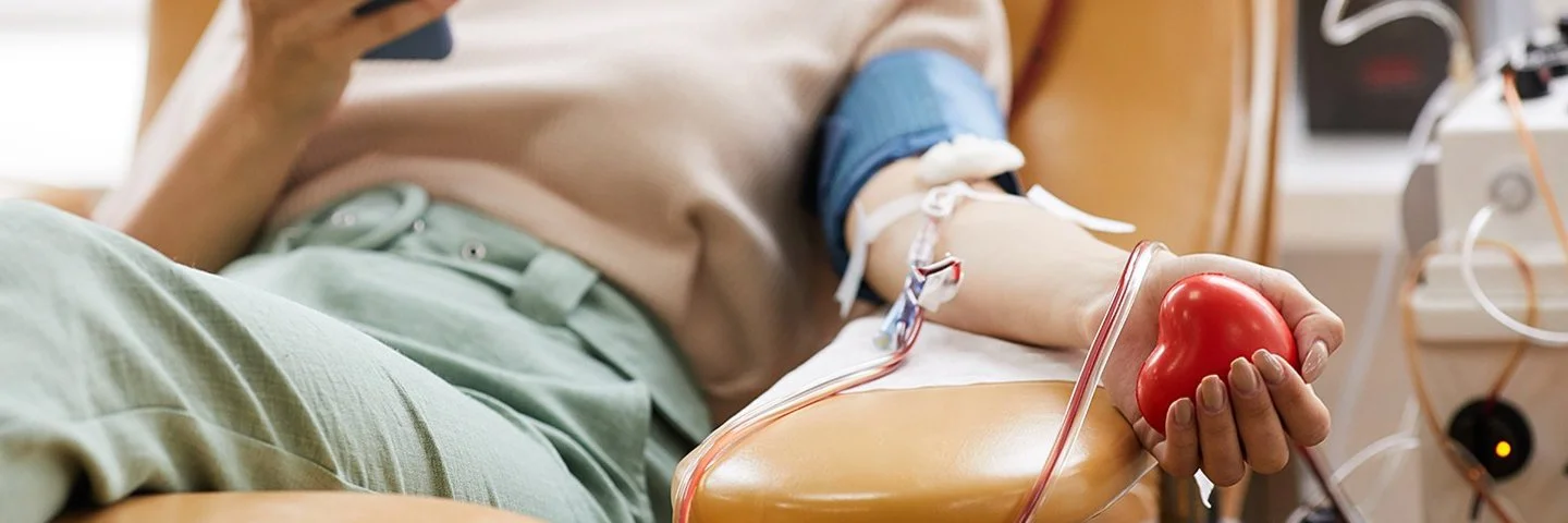 Eine Frau liegt auf einer Liege und spendet Blut. Dabei hält sie ihr Smartphone in der Hand.