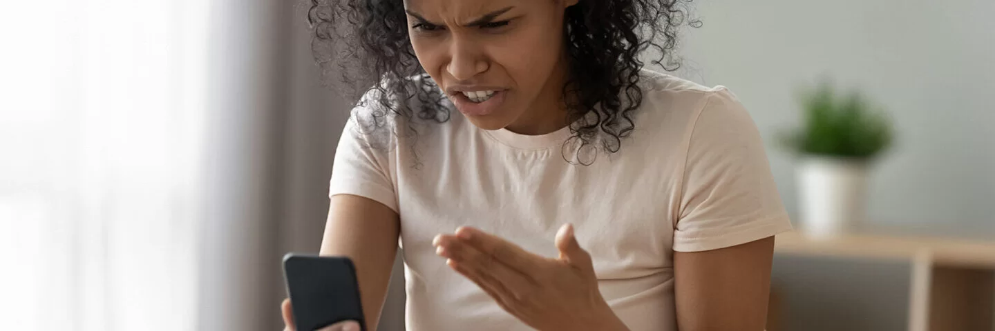 Frau mit Handy in der Hand ist wütend über Hate Speech.