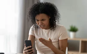 Frau mit Handy in der Hand ist wütend über Hate Speech.