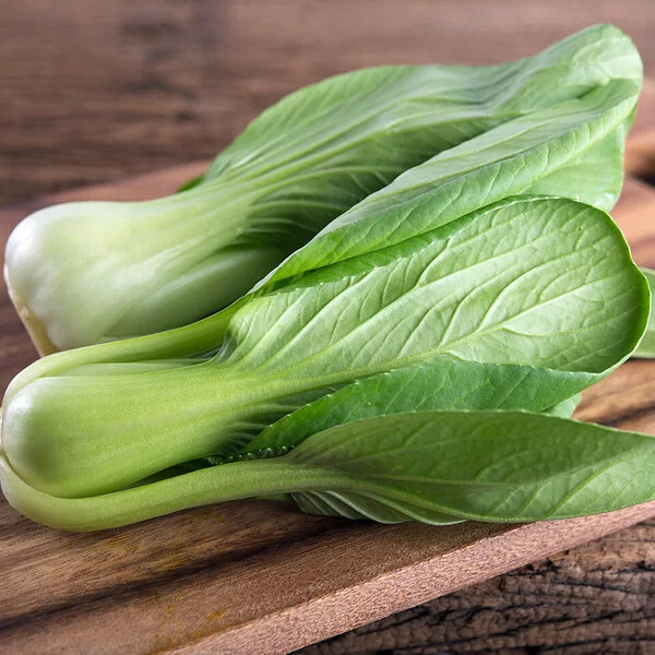 Zwei Baby-Pak-Chois liegen auf einem Holzschneidebrett auf einem Holztisch.